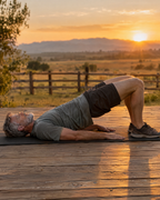 Man doing a glute bridge core exercise on a deck at sunrise